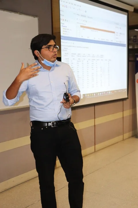 Presenting beside a projected data grid, hand raised mid-point